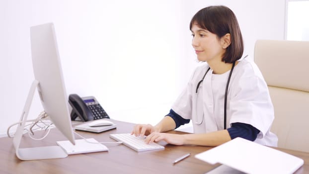 Concentrated female doctor using computer sitting on a desk in a clinic