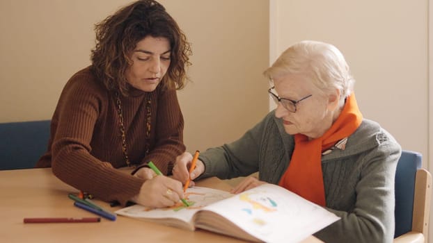 Female caregiver and senior woman coloring a draw in a geriatric