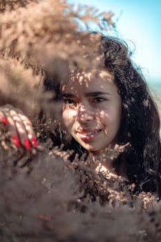 A woman is standing in a field of brown leaves. She is looking at the camera with a serious expression