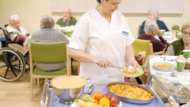 Cook serving pasta at the seniors sitting in geriatric dinning room