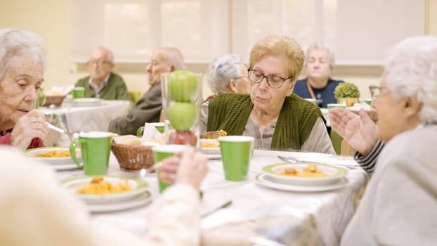 Group of senior women eating and talking sitting in geriatric's dinning room