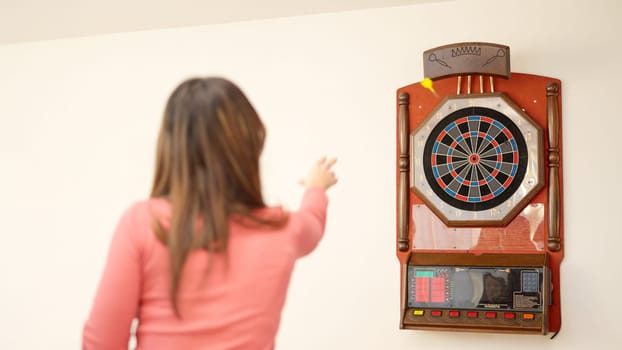 The rear view of a young caucasian woman playing darts at home