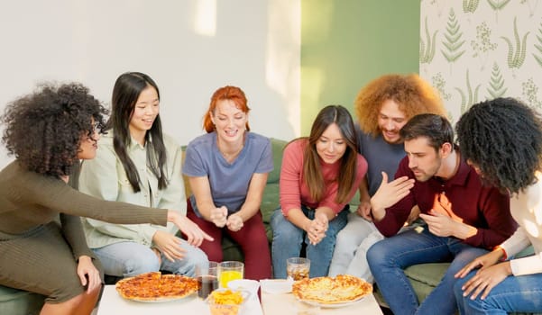 Multiracial group of happy friends chatting and eating pizza at home