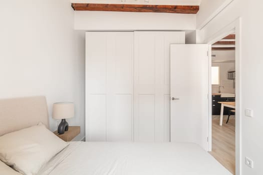 Closet and comfortable double bed in white bedroom minimalist design. Home residence interior with place to rest and wardrobe. House design