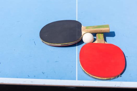 Red and black Table Tennis Paddles and ball on the blue table tennis table with net. Ping Pong concept with copy space. High quality photo