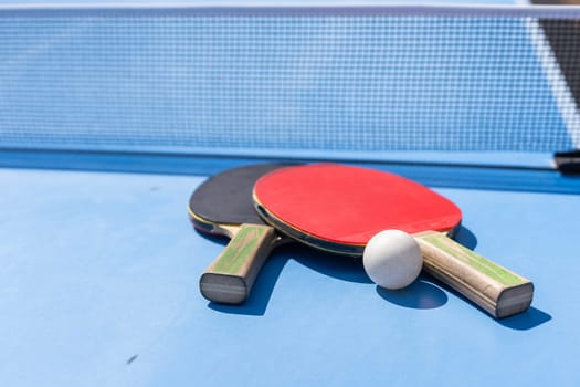 Two table tennis or ping pong rackets and ball on blue table with net. High quality photo