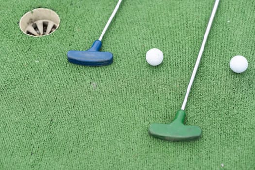 Mini-golf clubs and balls of different colors laid on artificial grass. High quality photo
