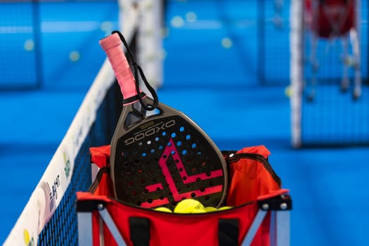 Kyiv, Ukraine, April 18, 2024. Black professional paddle tennis racket and ball with natural lighting on blue background. Horizontal sport theme poster, greeting cards, headers, website and app. High quality photo