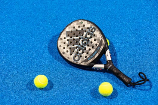 Kyiv, Ukraine, April 18, 2024. Black professional paddle tennis racket and ball with natural lighting on blue background. Horizontal sport theme poster, greeting cards, headers, website and app. High quality photo