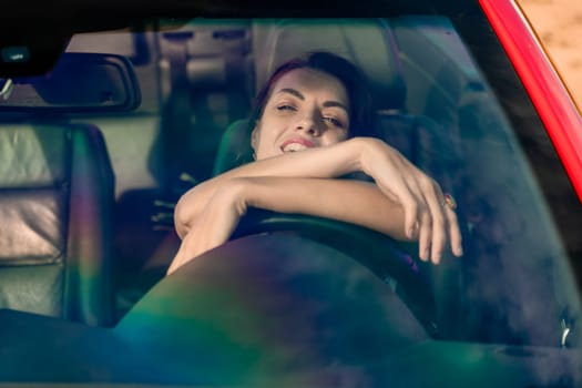 A woman is laying in a car with her hands on her face. She is smiling and she is relaxed