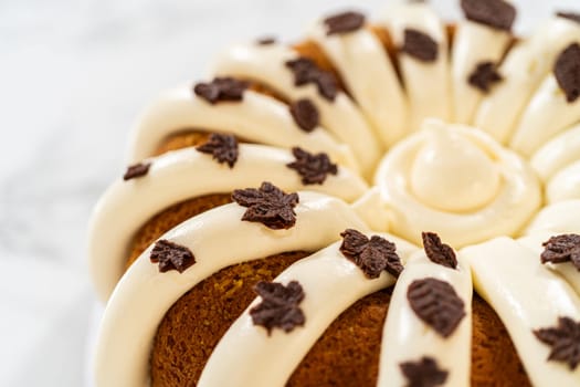 Icing the pumpkin bundt cake with cream cheese frosting and decorating it with chocolate leaves.