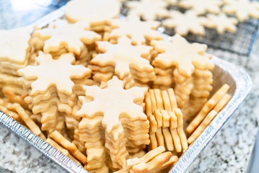 Carefully stacking the beautifully crafted snowflake-shaped sugar cookies into a foil pan, ready for freezing as delightful Christmas treats.
