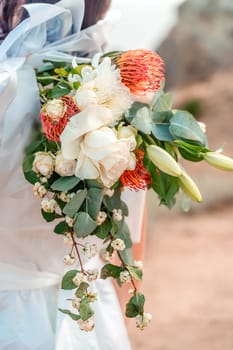 A woman is holding a bouquet of flowers, with a white dress and a bow. The flowers are a mix of red and white