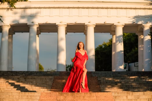 A woman in a long red dress against the backdrop of sunrise, bright golden light of the sun's rays. The concept of femininity, harmony