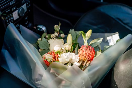 A bouquet of flowers is sitting in a car. The flowers are white and red, and they are in a clear plastic bag
