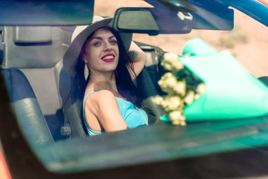 A woman is driving a car with a bouquet of flowers in the back seat. She is wearing a hat and has her eyes closed