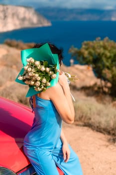 A woman is sitting on a red car with a bouquet of flowers in her hand. The flowers are white and green, and the woman is wearing a blue dress. The scene has a peaceful and serene mood