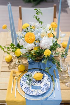 Name card lies next to an olive branch and a lemon on a plate on a set table near a colorful bouquet of flowers. High quality photo