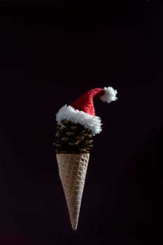 A cone shaped ice cream cone with a red hat on top. The cone is made of pine cones and the hat is made of white and red fabric