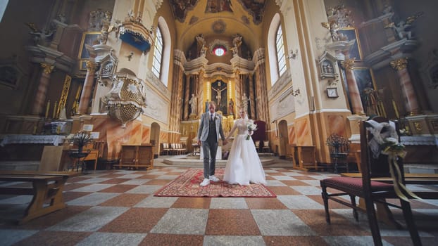 The bride and groom walk and kiss through a Catholic church