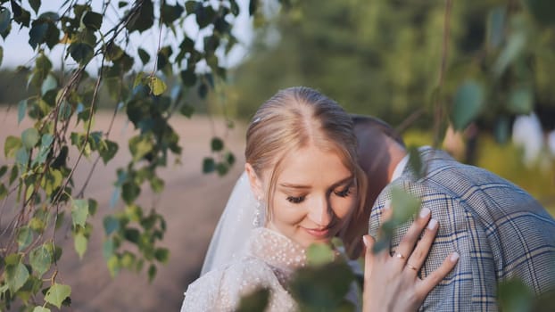 Bride and groom touching and enjoying each other against a backdrop of birch tree branches