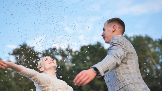 The bride and groom toss confetti above them and embrace