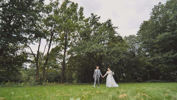 The bride and groom walk against a backdrop of dense trees