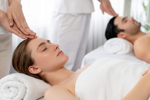 Caucasian couple enjoying relaxing anti-stress head massage and pampering facial beauty skin recreation leisure in dayspa modern light ambient at luxury resort or hotel spa salon. Quiescent