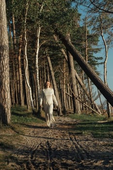 A woman is walking down a dirt road surrounded by tall trees on both sides.