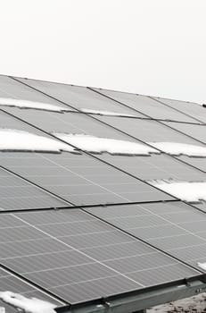 A row of solar panels sits on top of a roof covered in snow during winter.