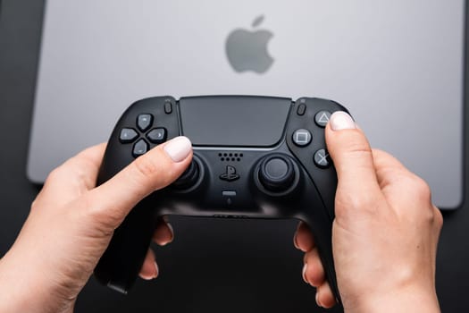 BERLIN , GERMANY - FEBRUARY 14 2024: Gaming joystick in womans hands over MacBook Pro