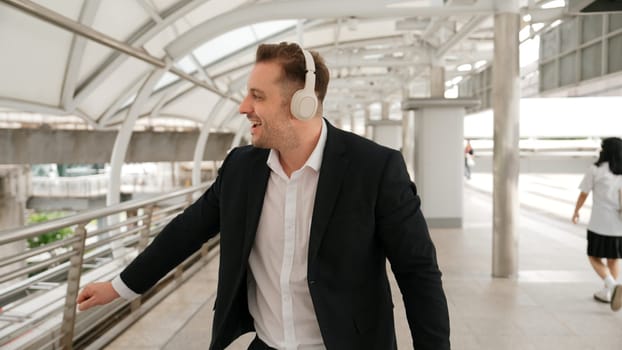 Happy business man dancing while wear headphone at bridge in urban city. Energetic manager cheerful and motivation performance moving to music to celebrate successful project while walk along. Urbane.