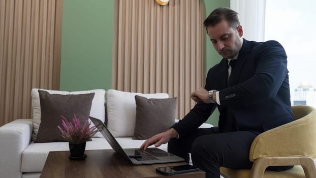 Businessman sitting on furniture working on laptop at ornamented corporate waiting area for meeting preparation. Office worker or business profession and strategic marketing plan for business success.
