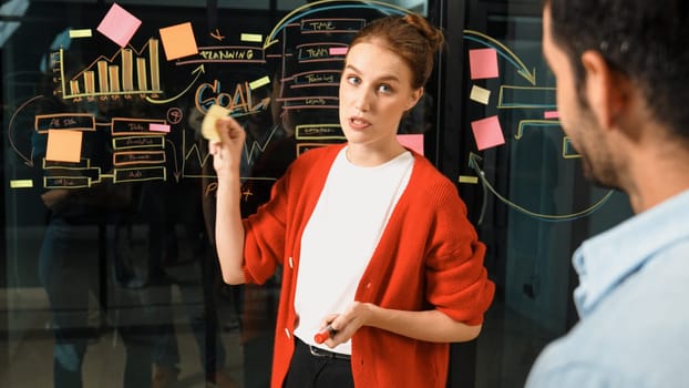 Closeup of young beautiful project manager present graph and business plan on glass wall. Skilled businesswoman show marketing strategy. Leader sharing brainstorming ideas to investor. Tracery
