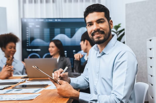 Portrait of happy and smiling businessman with group of coworkers on meeting with screen display business dashboard in background. Confident office worker at team meeting. Concord