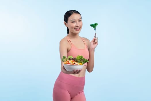 Young sporty Asian woman in sportswear holding salad bowl fill with vibrant of fruit and vegetable. Natural youthful and fit body lifestyle with balance nutrition on isolated background. Vigorous