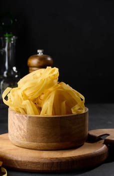 Raw long noodles made from white wheat flour in a wooden bowl on a black table