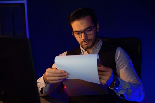 Serious smart businessman focusing on paperwork report folder analyzing sales channel discipline's product service comparing graph on pc screen market target customer at neon dark light room. Surmise.