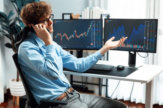 Young investor stock trader calling on smartphone to broker, discussing with dynamic financial exchange investment on two laptop screens in current market graph in real time at modern office. Gusher.