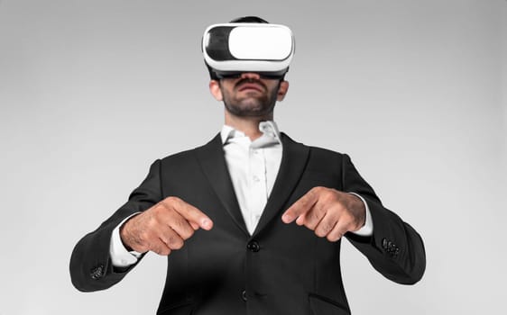 Smart business man wearing VR headset and suit while pointing at something. Caucasian investor connect mentaverse and virtual reality world while using VR goggles and standing. Innovation. Deviation.
