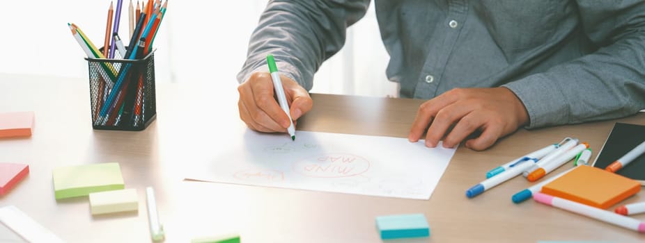 Skilled businessman brainstorms marketing ideas using mind maps. Successful male startup leader drafts financial plan on table with sticky notes scatter around. Closeup. Focus on hand.Variegated.