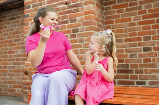 Child girl with cochlear implant with her mother spend time outdoor. Hear impairment and deaf community concept. Deaf and health concept. Diversity and inclusion. Copy space.