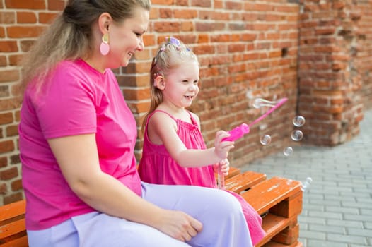 Blonde little girl with cochlear implant playing with her mother outdoor. Hear impairment deaf and health concept. Diversity and inclusion. Copy space.