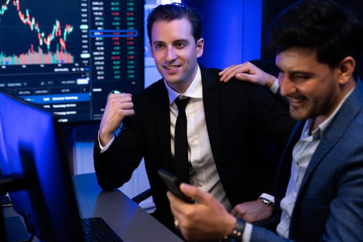Two stock exchange traders getting profit in trading currency stock. Successful stock exchange showing financial benefit data on monitor screen at highest point of neon light at workplace. Sellable.