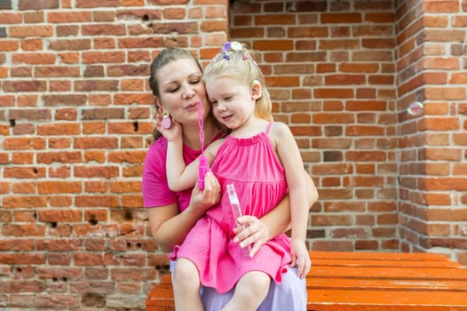 Blonde little girl with cochlear implant playing with her mother outdoor. Hear impairment deaf and health concept. Diversity and inclusion. Copy space.