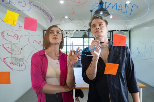 Couple of young creative start up business people brainstorming idea and solving problems by using sticky note and mind map at glass board, meeting room. discussing, working together. Immaculate.