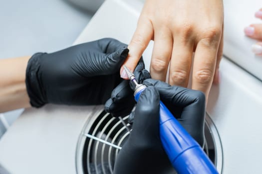 Manicurist uses an electric drill to remove old gel polish from nails. A woman is getting a manicure of nails. The beautician files the client's nails. professional manicure tool. Close-up.