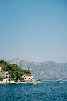 Boats stand off the coast of Perast with old houses among green trees. Montenegro. High quality photo
