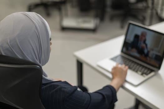 A pregnant woman in a hijab communicates with a colleague via video conference on a laptop