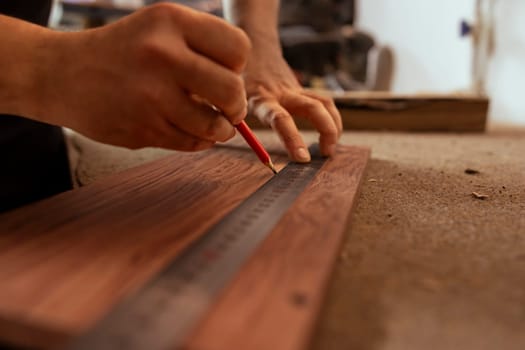 Craftsperson using ruler to take measurements of plank used to make wood furniture in carpentry shop. Woodworking expert drawing with pencil on wooden board to determine where to make cut, close up